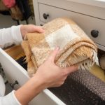 Person organizing folded plaid blanket in drawer with other knit items. Home organization and storage concept.